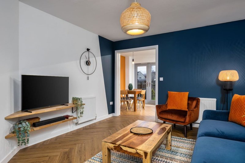 Modern living room with blue walls, wooden floor, TV, orange armchair and blue sofa