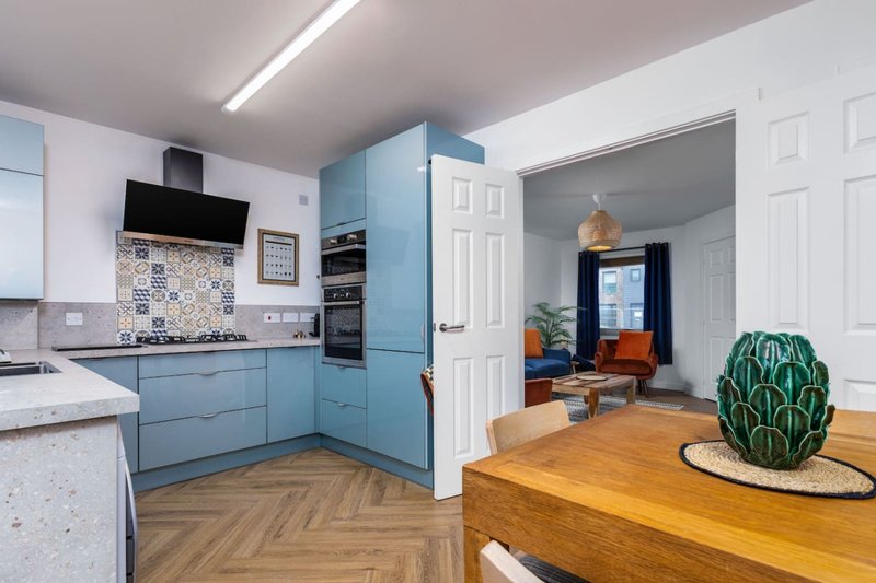 Modern kitchen with blue cabinetry, wooden dining table, and open-plan living area