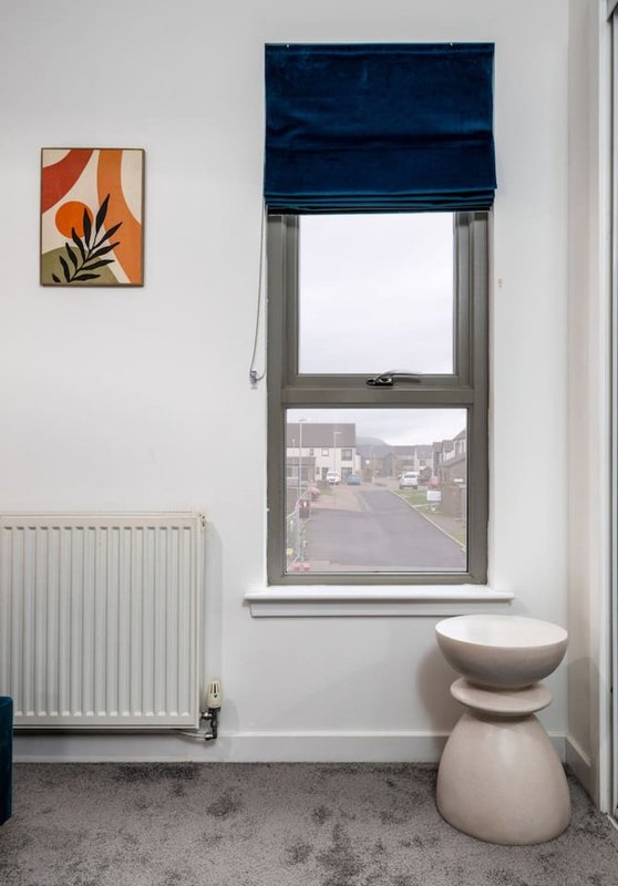 Bedroom window with blue blind, radiator, abstract wall art, and ceramic stool