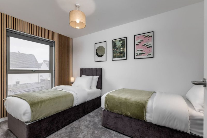 Twin bedroom with two single beds, modern pendant light, wooden wall paneling, and framed artwork