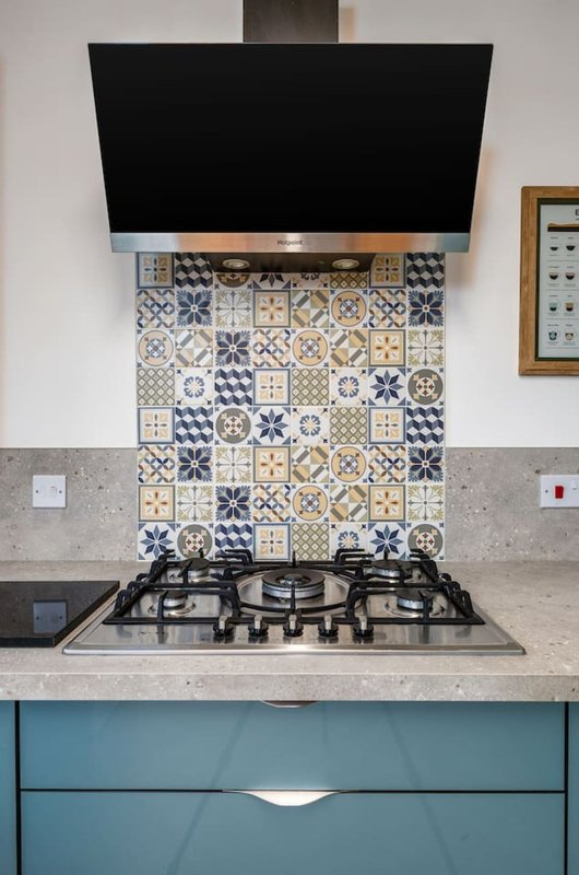 Modern kitchen with teal cabinetry, gas cooktop, patterned tile backsplash and black range hood