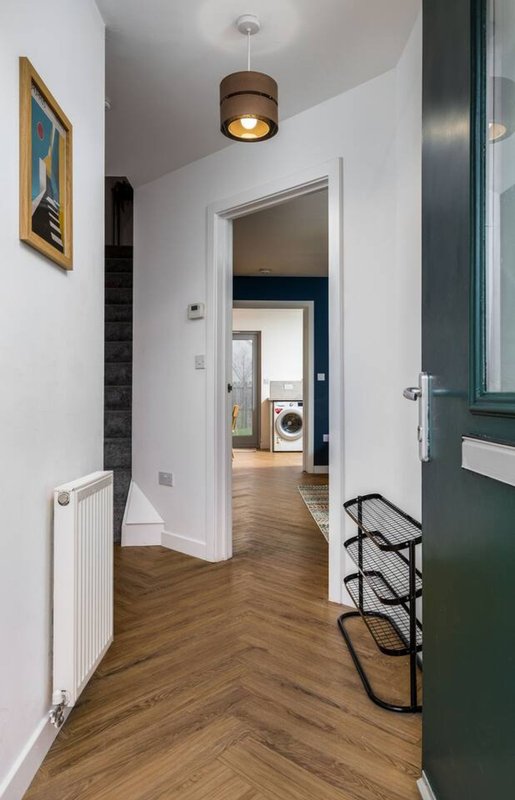 Modern hallway with wooden flooring, white walls, pendant lighting, and view into kitchen