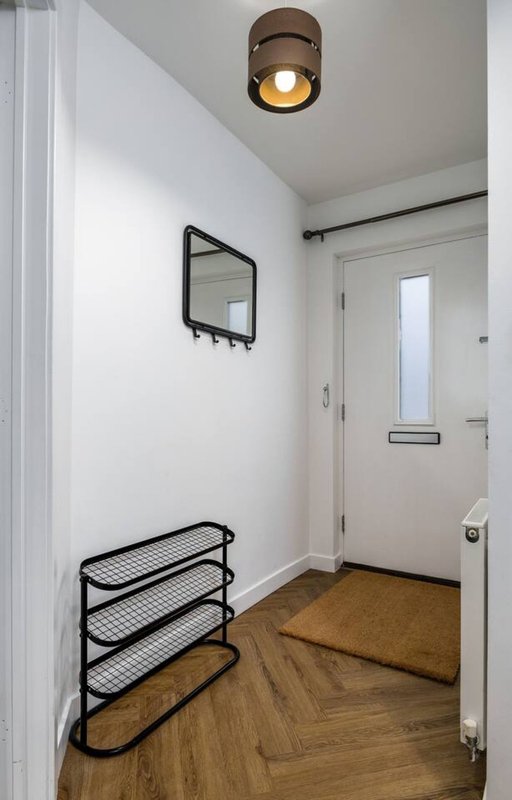 Bright entryway with wooden herringbone floor, wall-mounted mirror, metal shoe rack and ceiling light