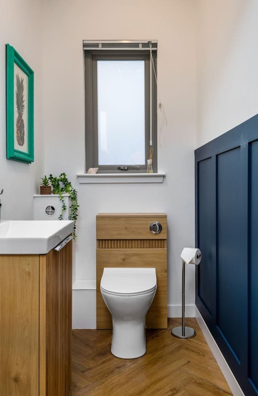Modern bathroom with toilet, wooden vanity, sink, window and green wall art