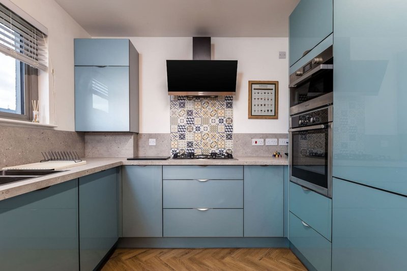Modern kitchen with blue cabinetry, stainless steel appliances, patterned backsplash and wooden flooring