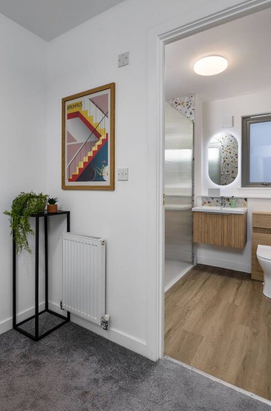 Modern hallway with framed artwork, plant stand, radiator, and open doorway to bathroom
