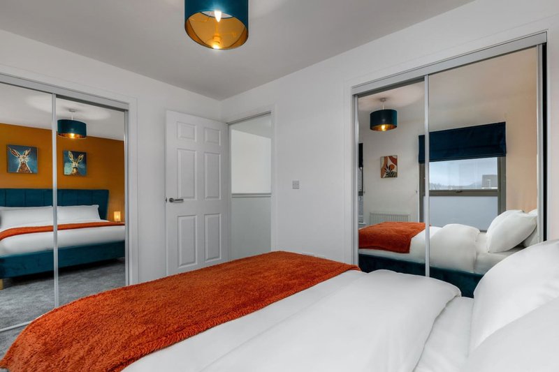 Modern bedroom with double bed, orange runner, mirrored wardrobe and pendant ceiling light