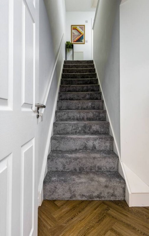 Staircase with grey carpet, white walls, wooden floor at base, and framed artwork on wall