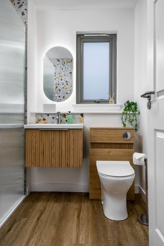 Modern bathroom with wooden vanity, toilet, oval mirror, and window