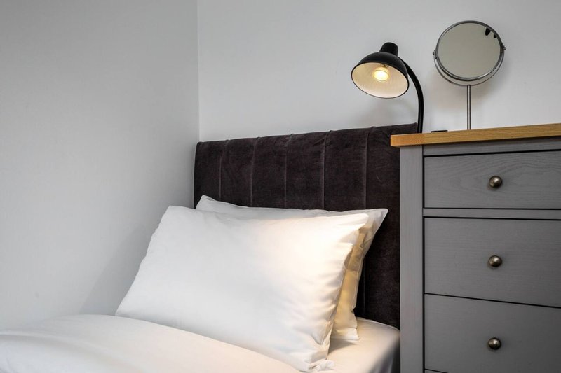 Bedroom with dark headboard, white pillows, grey bedside cabinet and reading lamp