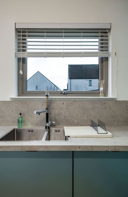 Modern kitchen with double sink, green cabinetry, and window overlooking neighboring houses