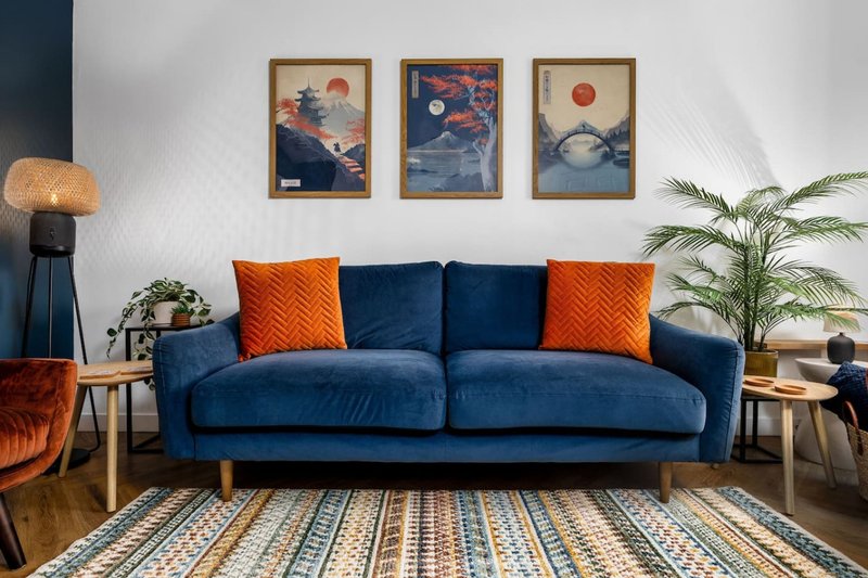 Modern living room with blue sofa, orange cushions, framed artwork, and potted plant