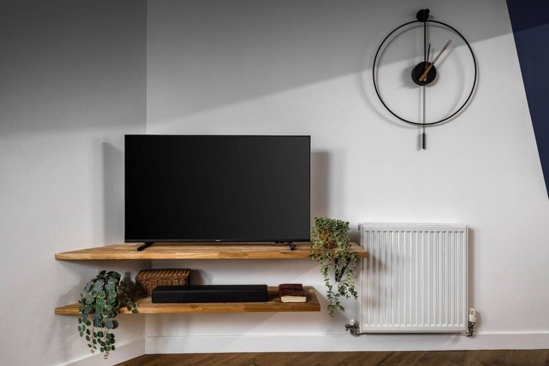 Modern wall-mounted TV setup with wooden shelves, potted plants, and round wall clock