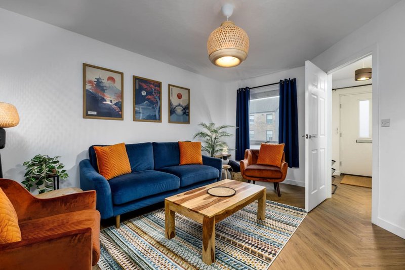 Modern living room with blue sofa, orange armchairs, wooden coffee table and framed artwork