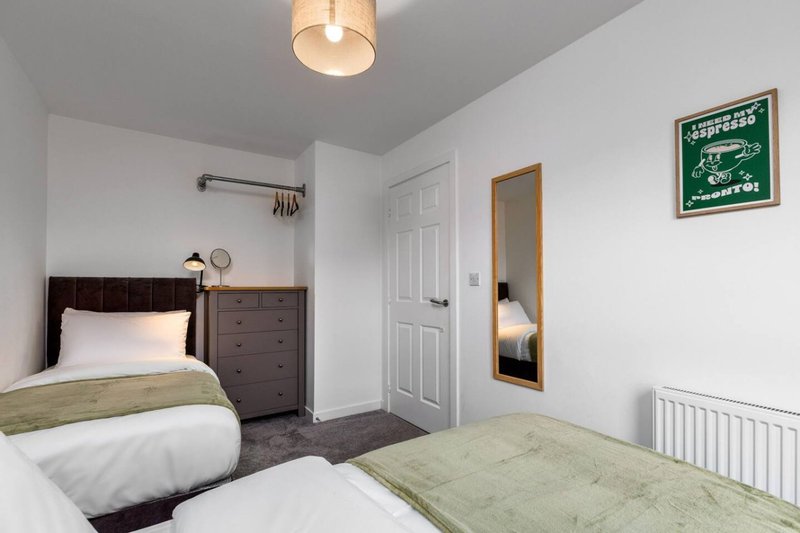 Modern bedroom with two single beds, dark headboards, chest of drawers, and wall-mounted mirror