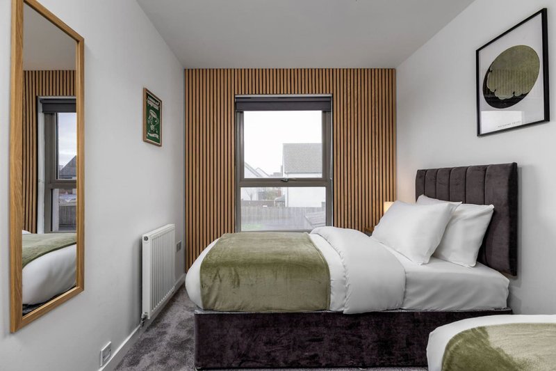 Modern bedroom with double bed, olive bedspread, dark headboard, and full-length mirror