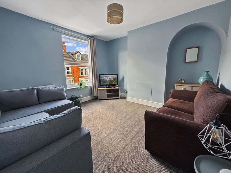 Living room with gray sofa, brown armchair, TV unit, and arched alcove with turquoise walls