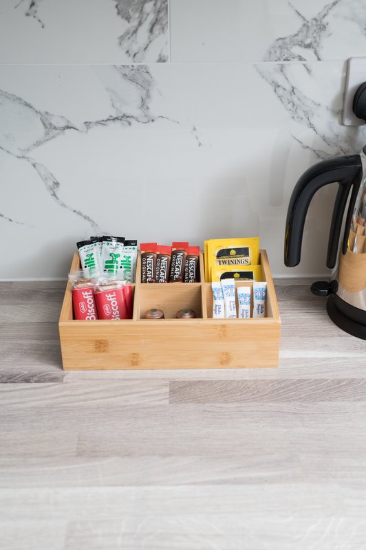 Kitchen counter with wooden organizer containing tea bags, batteries, and other small items