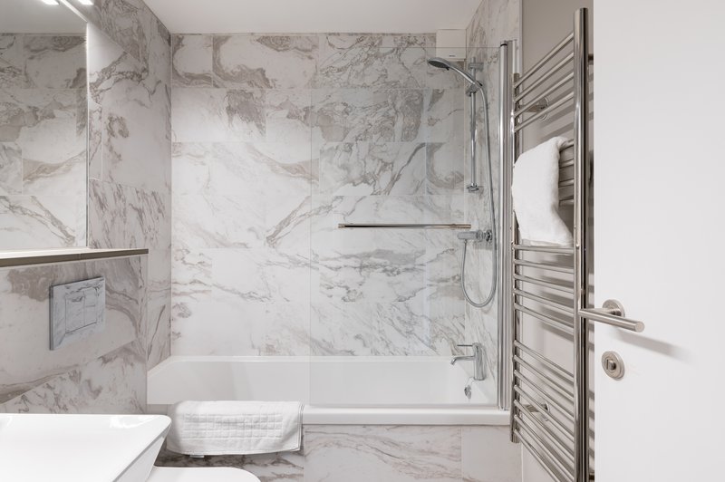 Modern bathroom with marble tiles, glass shower enclosure and heated towel rail