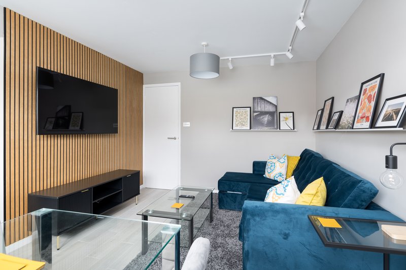 Modern living room with blue velvet sofa, wall-mounted TV, framed wall art and track lighting