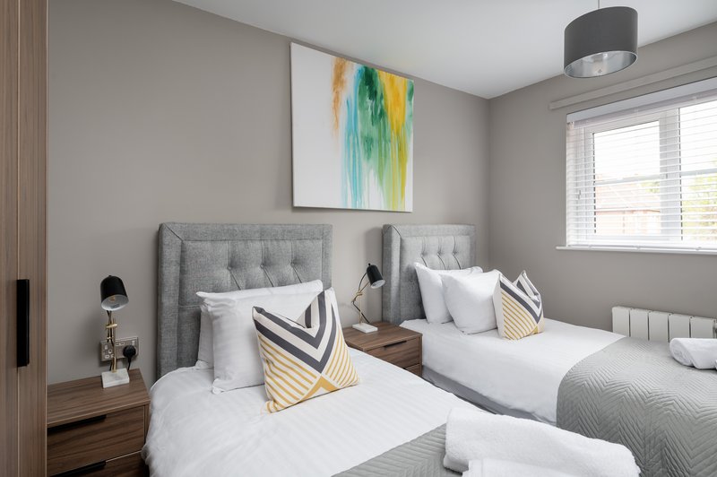 Modern twin bedroom with grey upholstered headboards, white bedding, decorative pillows and artwork