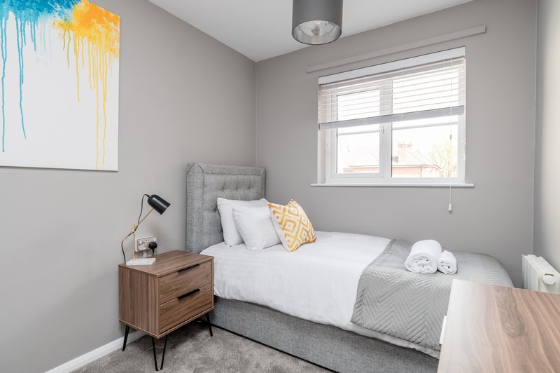 Modern bedroom with gray upholstered bed, wooden nightstand, white bedding and abstract wall art