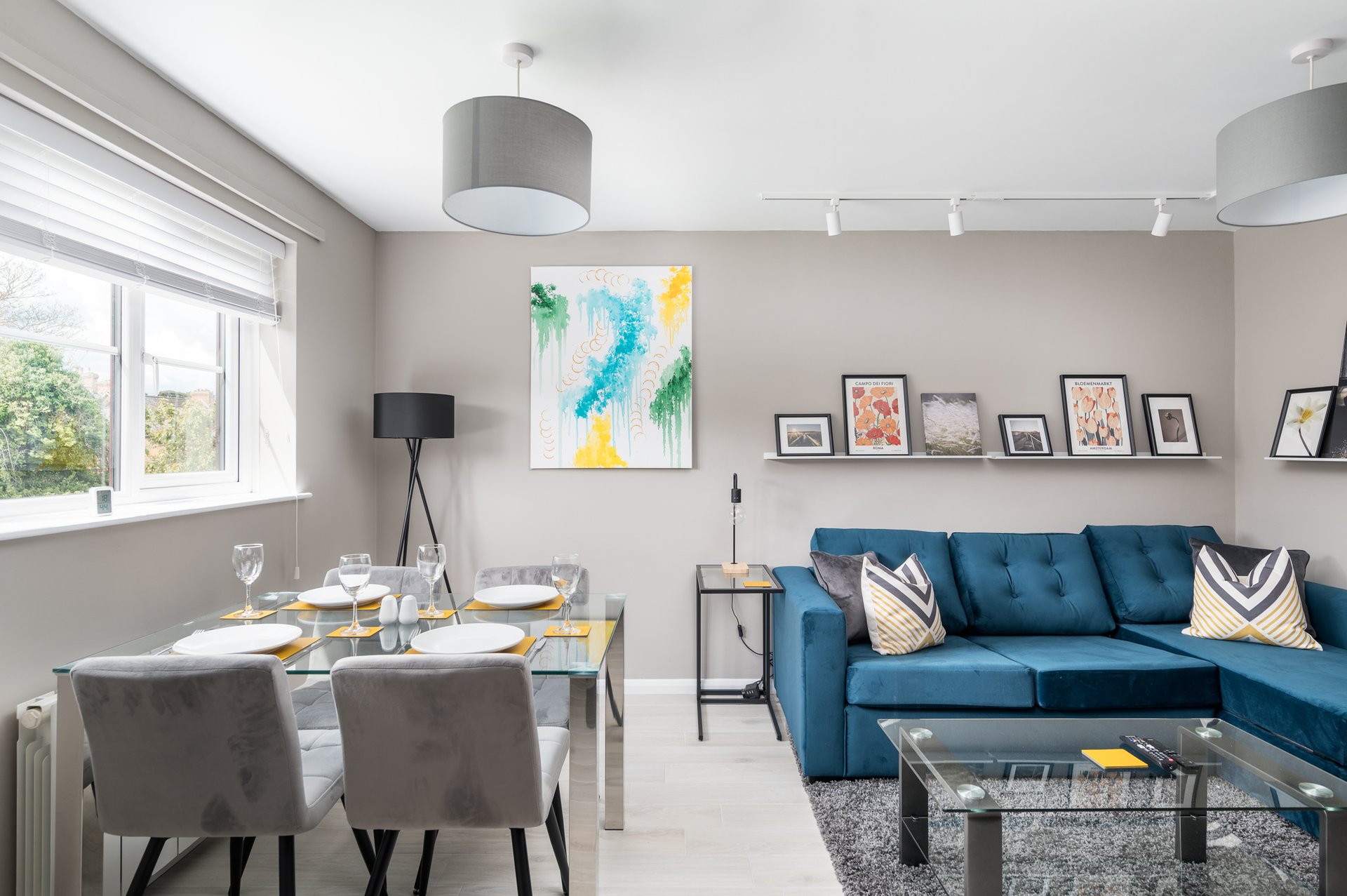 Open-plan living and dining area with blue sofa, dining table, framed artwork and pendant lighting