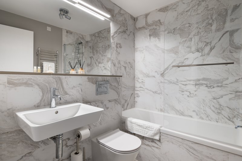 Modern bathroom with marble tiles, white sink, toilet, bathtub and mirror