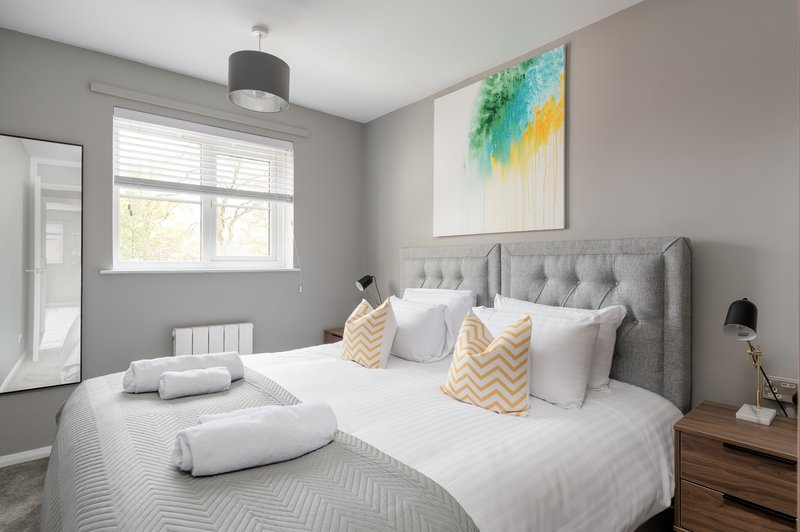 Modern bedroom with gray upholstered bed, white bedding, decorative pillows and artwork