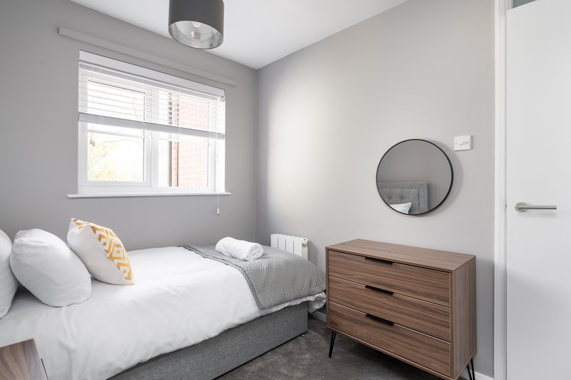 Bright bedroom with single bed, wooden dresser, round mirror and window