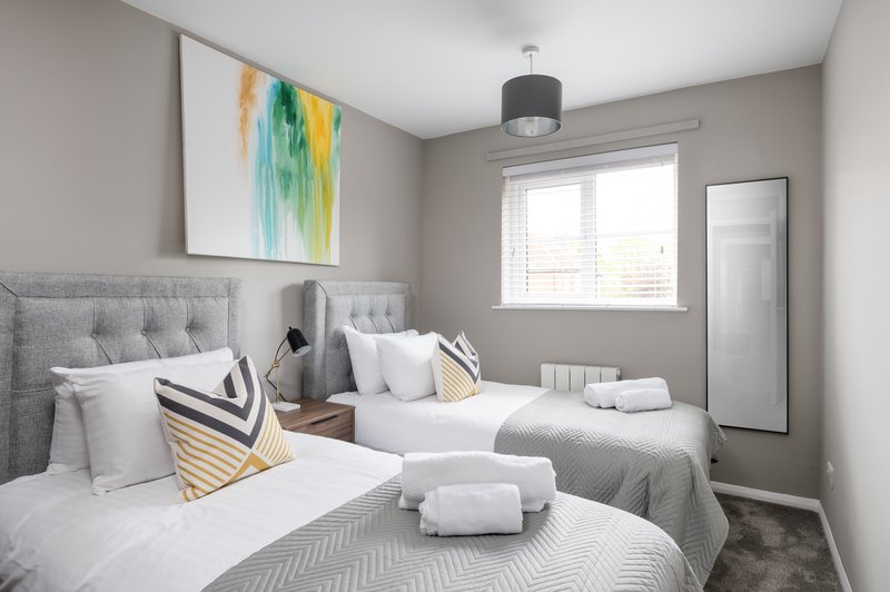 Modern bedroom with two twin beds, gray upholstered headboards, white bedding and colorful wall art