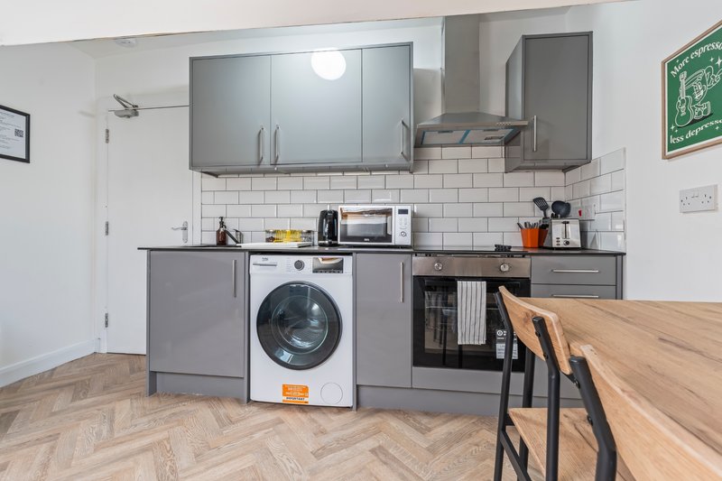 Modern kitchen with gray cabinets, white subway tiles, washing machine, and wooden dining table