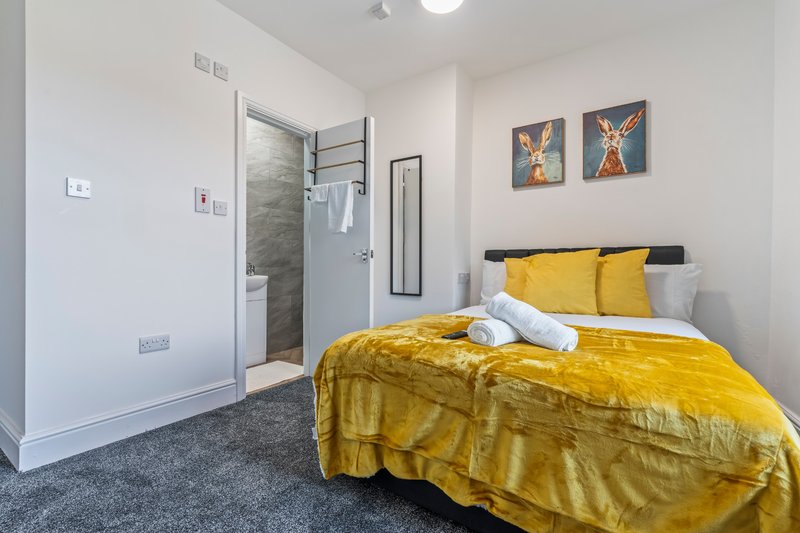 Modern bedroom with yellow bedding, ensuite shower room, and wall art