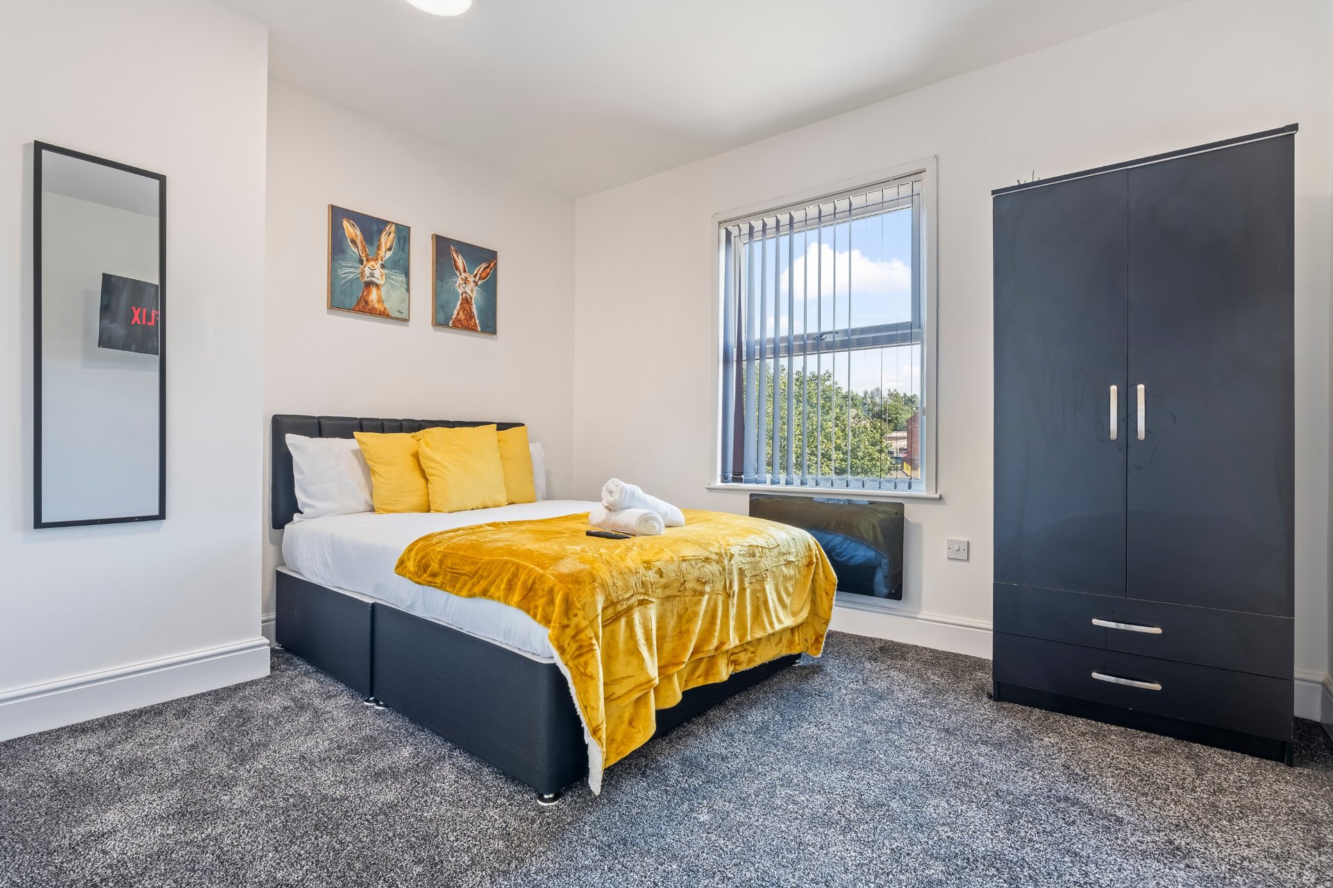Modern bedroom with double bed, yellow bedding, dark wardrobe, and window with countryside view
