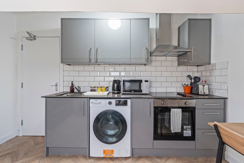 Modern kitchen with gray cabinetry, white subway tile backsplash, integrated appliances and wooden dining table