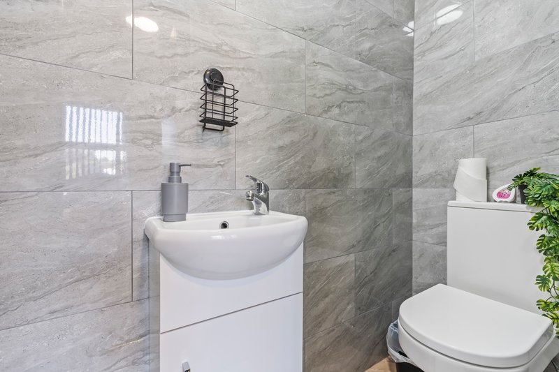 Modern bathroom with white vanity sink, toilet, grey tile walls and shower enclosure