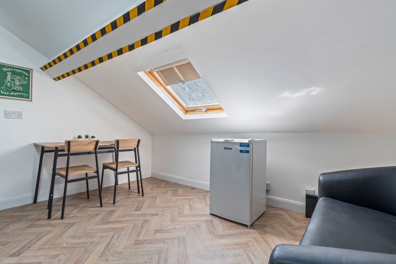 Attic room with dining table, chairs, skylight, wooden floor and grey appliance