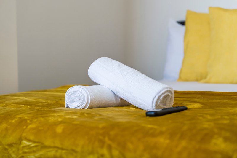 Rolled white towels arranged on yellow bedcover with matching pillows
