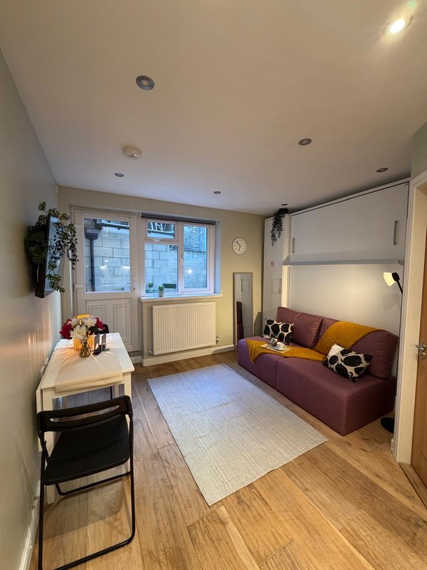 Studio apartment with sofa, small dining table, windows and wooden flooring