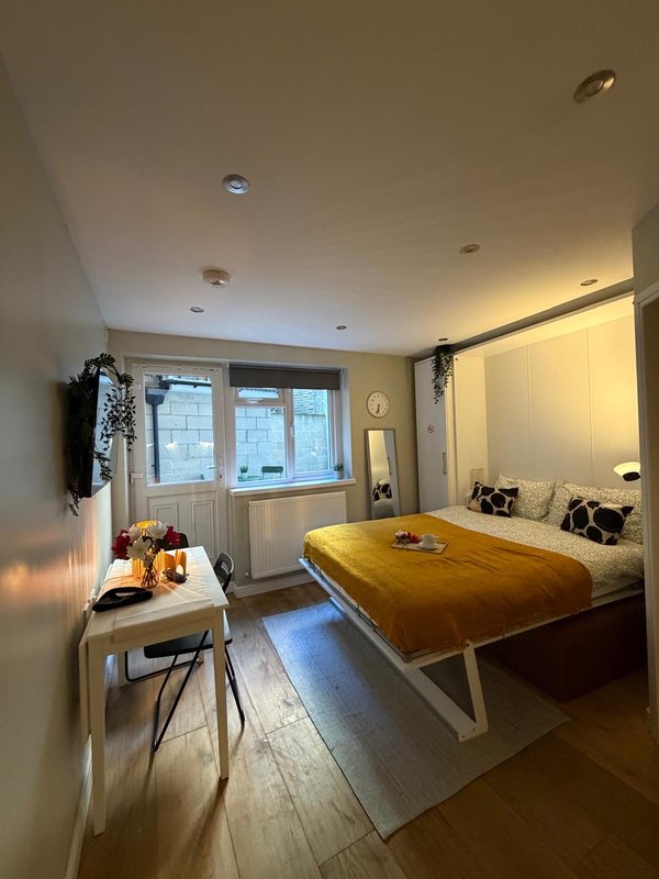 Bright modern bedroom with double bed, wooden desk, chair, and large windows overlooking street