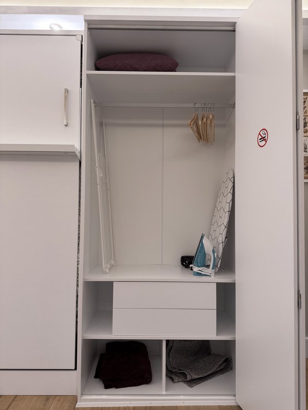 Open wardrobe with shelves, hanging rail, ironing board and folded clothes