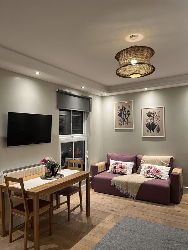 Living room with purple sofa, wooden dining table, wall-mounted TV, and framed artwork