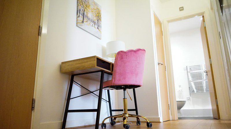 Compact home office corner with wooden desk, pink upholstered chair and wall art