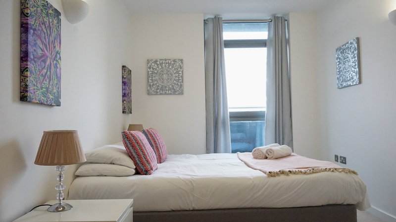 Modern bedroom with double bed, decorative pillows, wall art, and balcony access