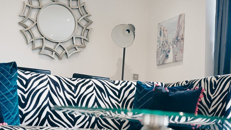 Modern bedroom with zebra-patterned sofa, decorative wall mirrors, and teal curtains