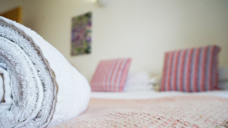 Rolled white towel in foreground, bedroom with pink striped cushions and wall art