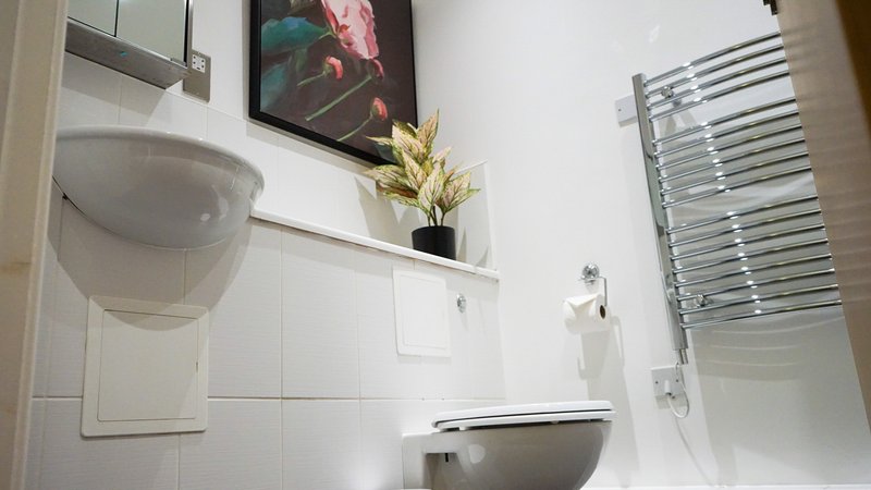 Modern bathroom with white tiles, wall-mounted sink, toilet, heated towel rail and shelf decor