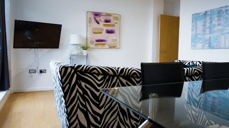 Modern living room with zebra-print sofa, glass table, wall-mounted TV and artwork