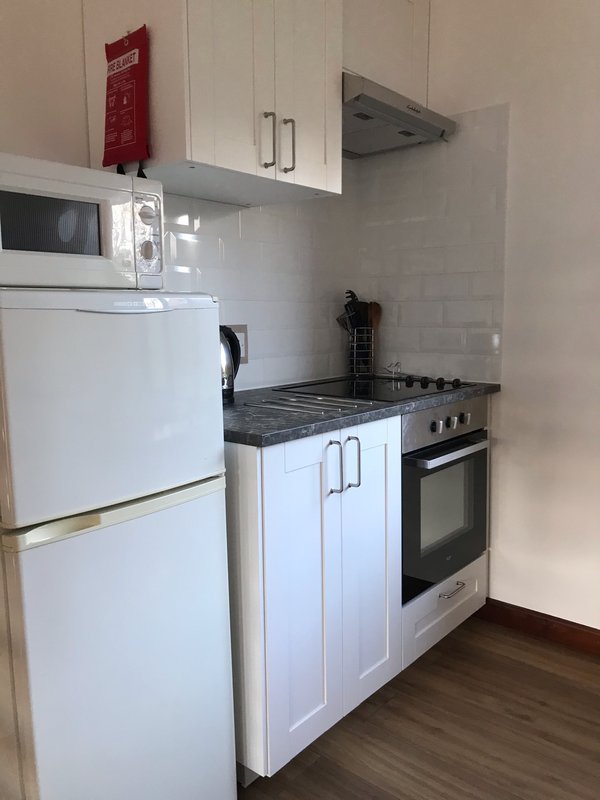 Modern kitchen with white cabinets, stainless steel appliances, black countertop and wooden floor
