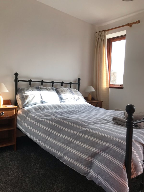 Bedroom with double bed, black metal frame, striped bedding, wooden nightstands and window with curtains